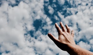 En hånd rækker op mod en overskyet himmel En hånd rækker op mod en overskyet himmel