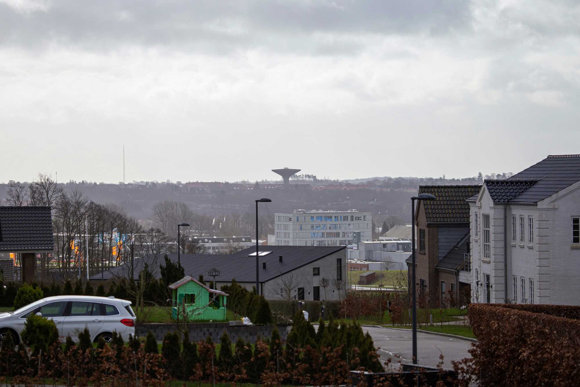 En bil holder parkeret ved hus, i baggrunden ses en tom legeplads og udsigt til vandtårnet i Næstved Nord