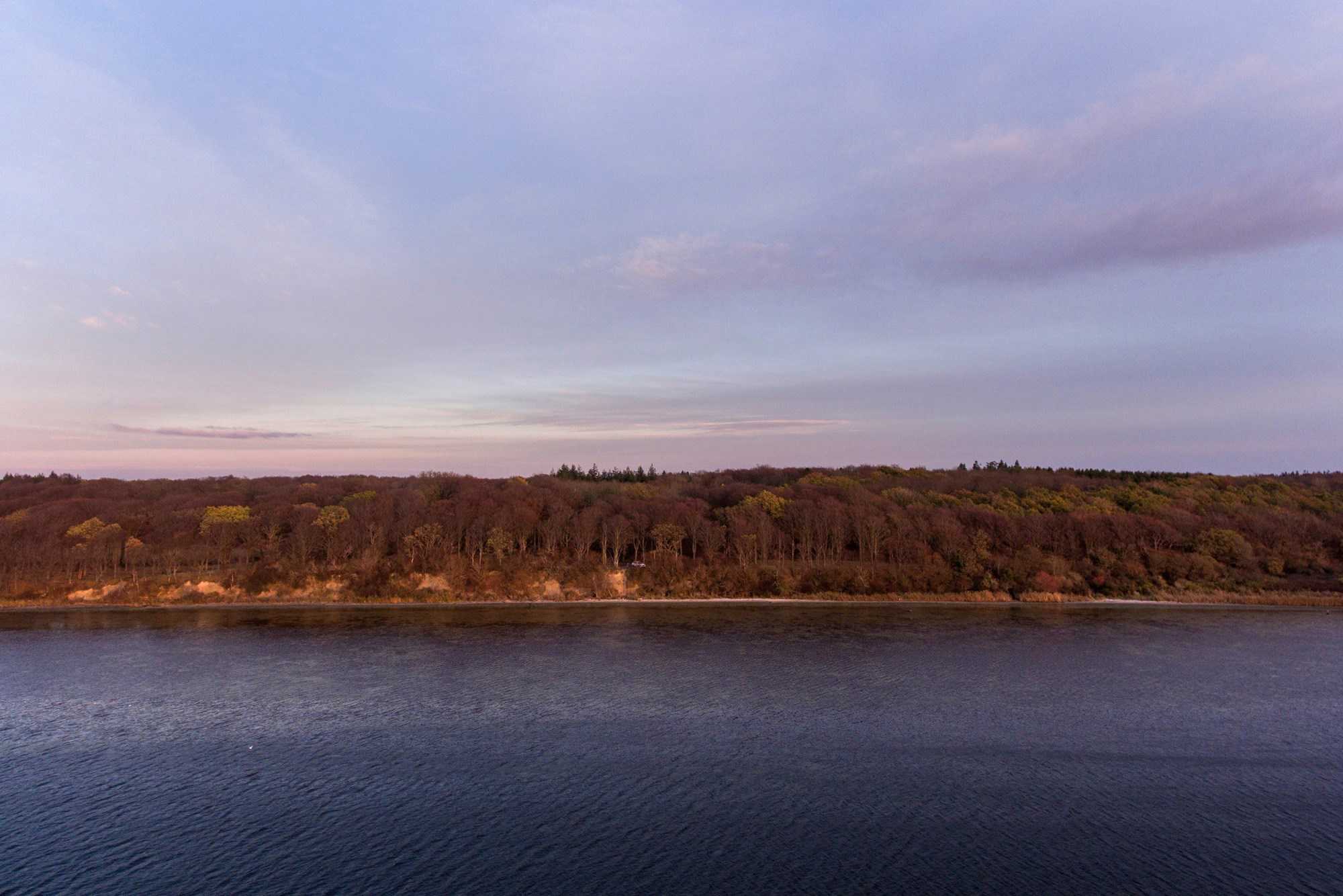 Rødlig himmel, skov og vand