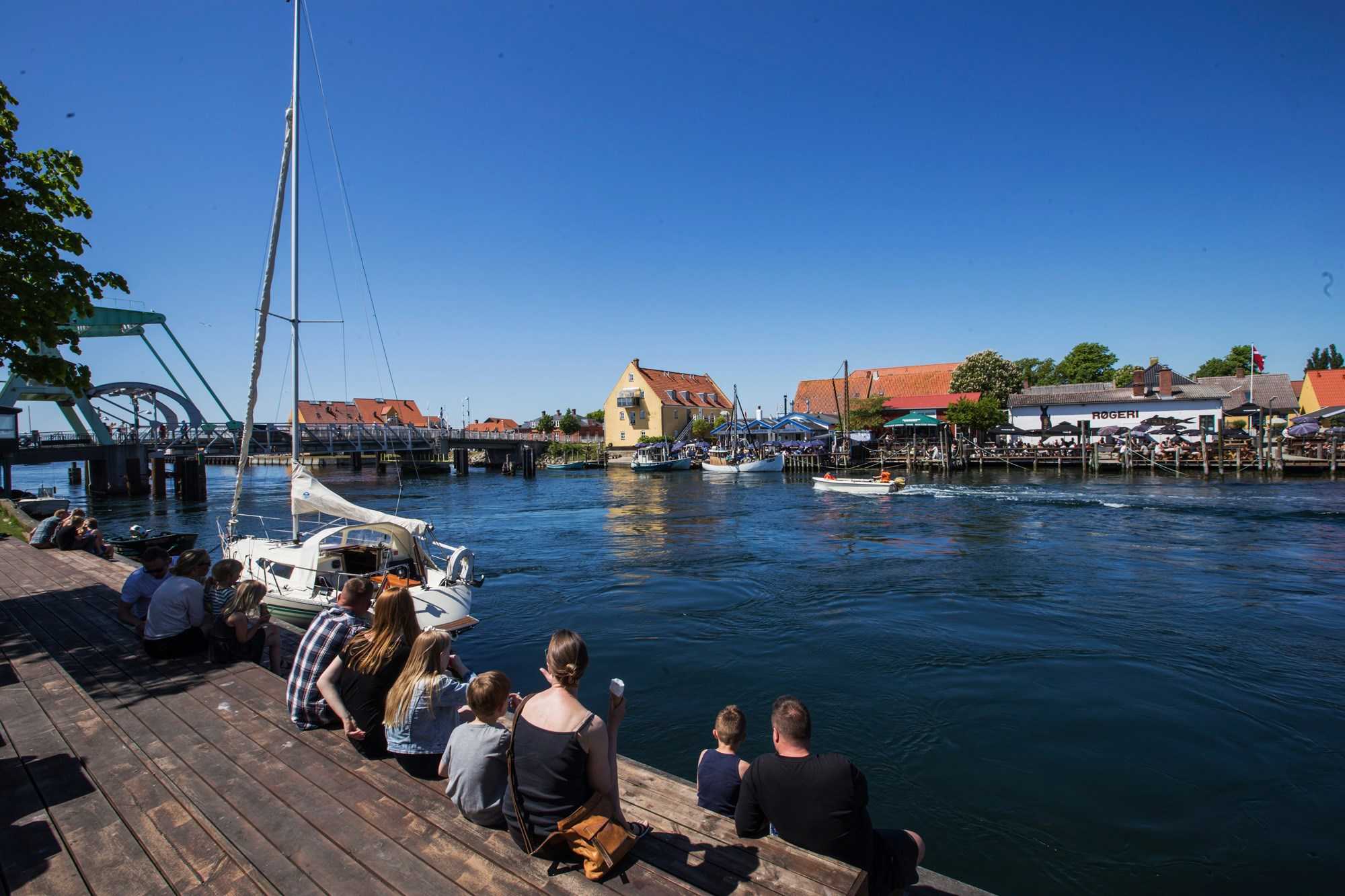 Børn og voksne sidder sammen ved fjorden i Karrebæksminde og ser ud på vandet