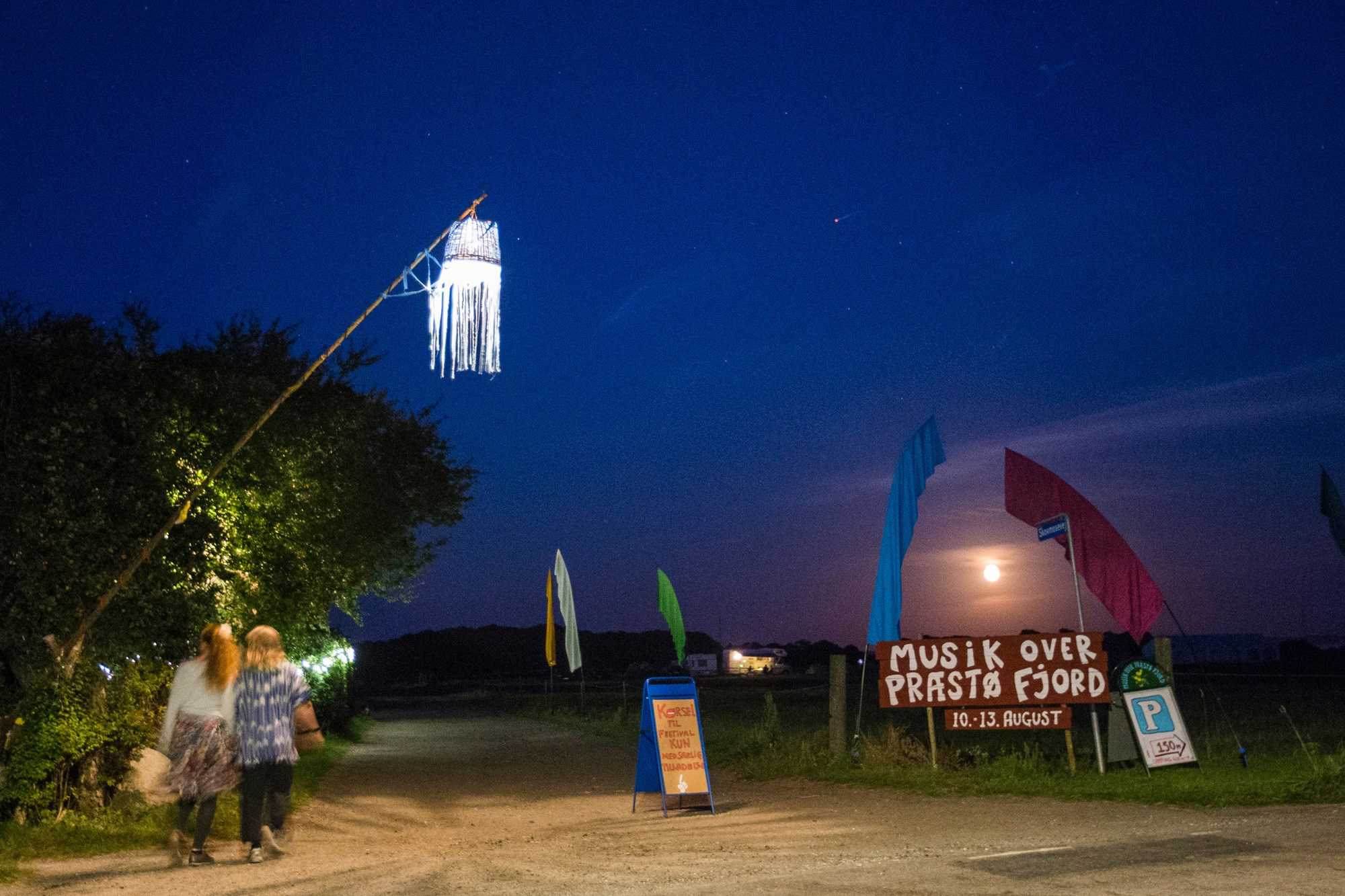 To piger på vej ned ad en sti hvor et skilt annoncerer Musik Over Præstø Fjord