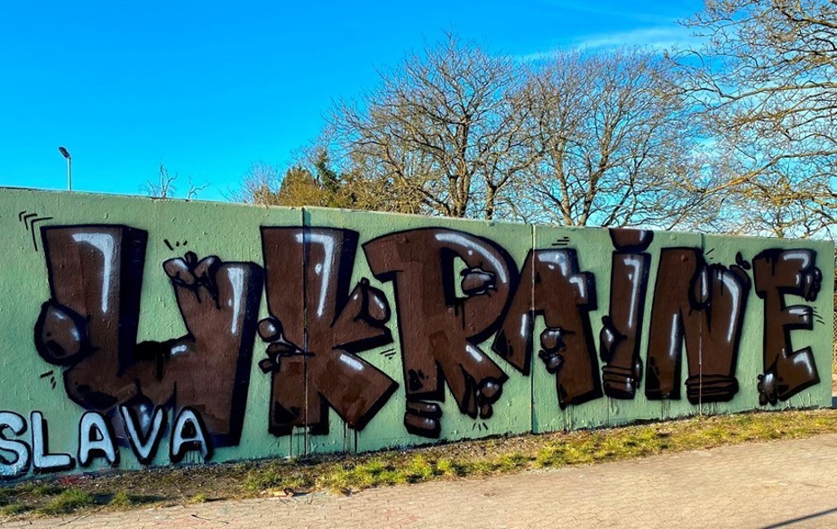 Grafitti-værk med teksten "Slava Ukraine" og blå himmel med hvidlige skyer