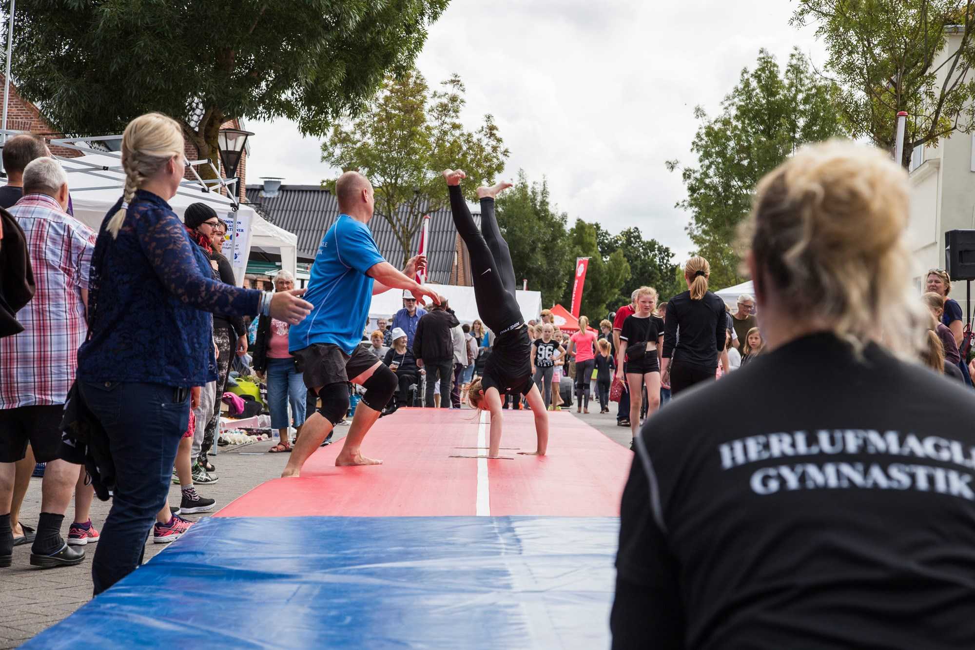 Pige midt i spring på gymnastikmåtte med træner der tager imod