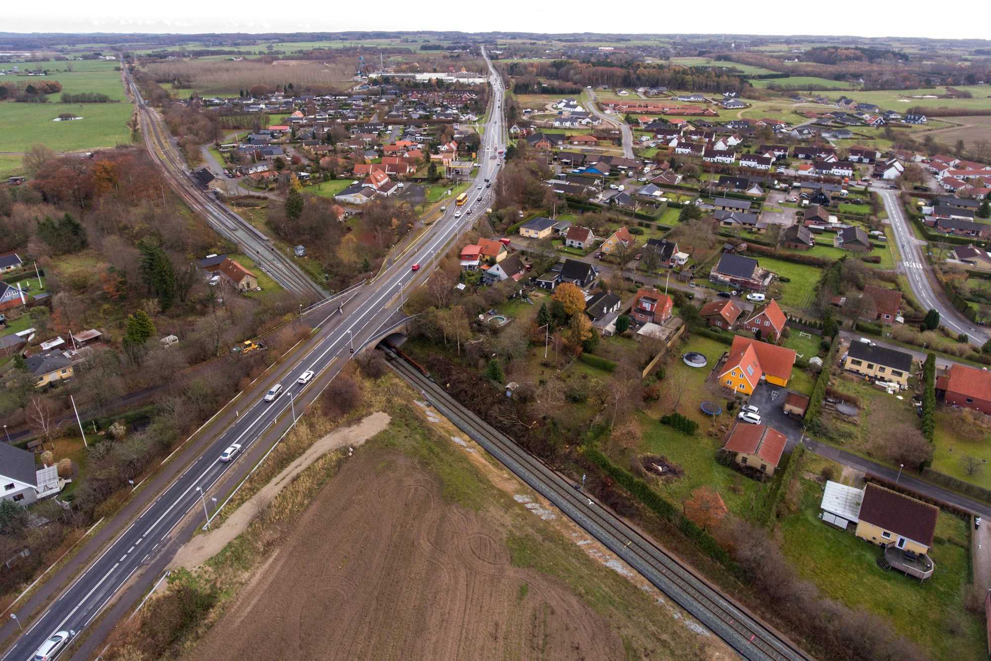 Dronefoto over Holme Olstrup hvor togskinner og landevej krydser igennem byen